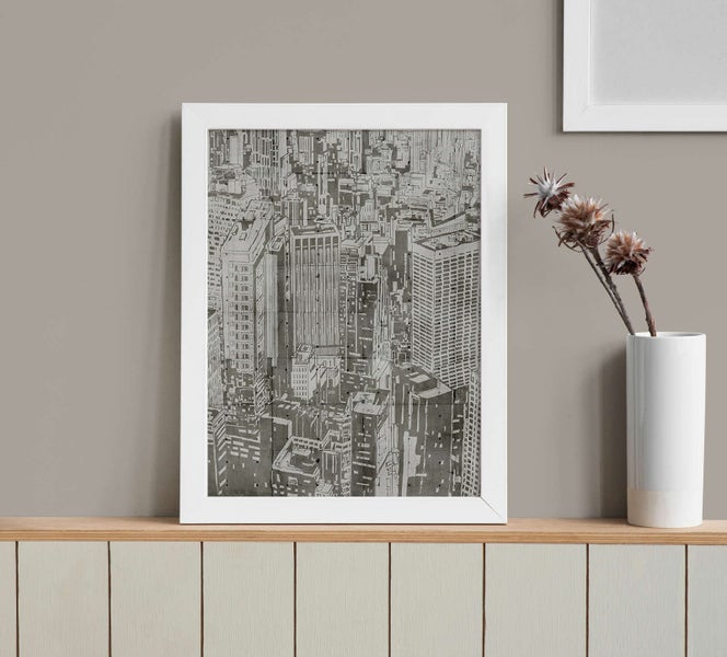 Gerahmtes Bild mit einer schwarz-weißen Zeichnung einer Skyline in einem weißen Rahmen auf einem Regal.