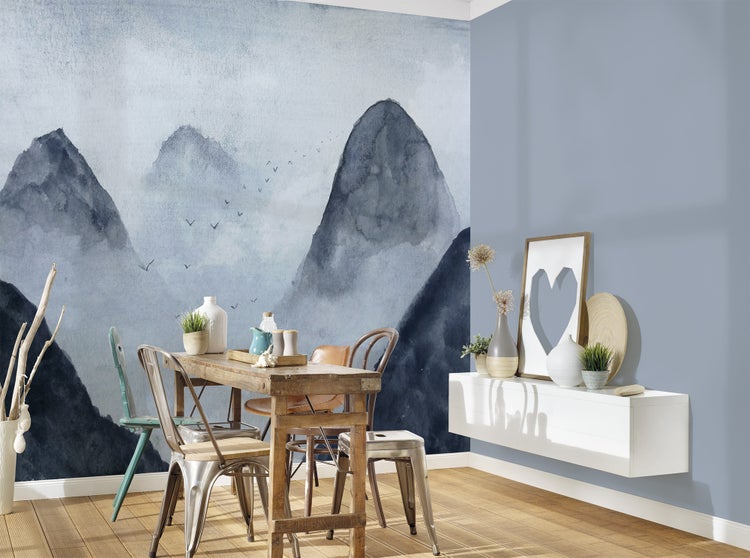Modernes helles Esszimmer mit Fototapete im Aquarell-Stil mit Bergmotiv, rustikalem Holztisch, verschiedenen Stühlen aus Metall und Holz.
