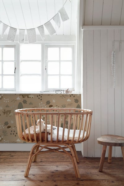 Blick auf ein Kinderzimmer mit einem Stubenwagen aus Rattan, einer Fensterdekoration mit Flaggen und einer Waldtapete.