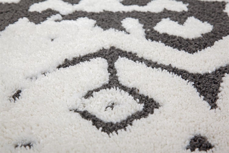 Detailaufnahme eines Hochflor-Shaggy-Teppichs mit weißem und grauem geometrischem Muster.