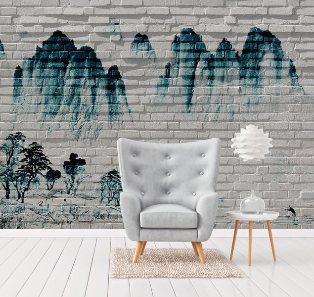 Fototapete mit Berglandschaft in Tuscheoptik auf einer Backsteinwand, kombiniert mit Sessel und Beistelltisch in hellem Wohnraum.