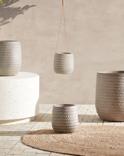 Verschiedene Pflanzgefäße mit Flechtmuster auf einem Teppich und einem Sockel
