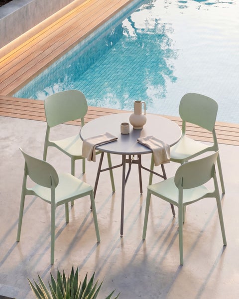 Modernes Gartenmöbel-Set bestehend aus einem runden Tisch und vier Kunststoffstühlen neben einem Swimmingpool auf einer hellen Terrasse.