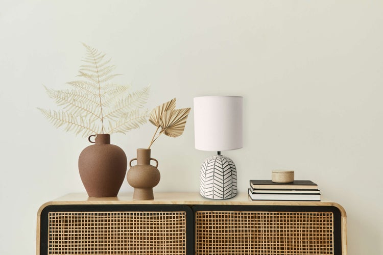 Dekorative Szene auf einem Holzschrank mit Vasen, Trockenblumen, einer Lampe, Büchern und einer Dose