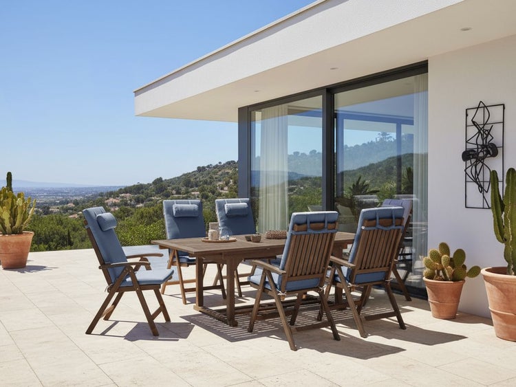 Moderne Garten-Essgruppe aus Holz auf einer hellen, geräumigen Terrasse mit sechs Klappstühlen inklusive Polsterauflagen vor weitem Ausblick.