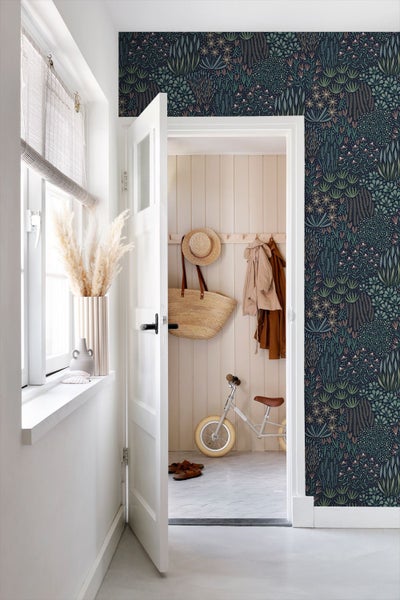 Heller Flur mit dunkler botanischer Tapete mit Pflanzenmotiven, offener weißer Tür zu einem Raum mit Holzpaneelen und Laufrad.