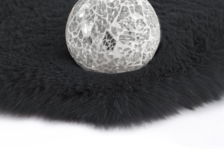 Dekorative Mosaikkugel aus Glas auf einem flauschigen Kunstfellteppich mit langem Flor.
