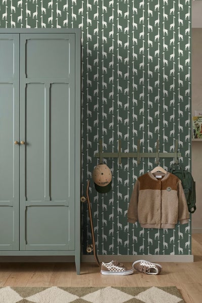 Kinderzimmer mit Giraffenmuster-Tapete, grünem Kleiderschrank, Garderobenleiste mit Jacke, Skateboard und Schuhen auf Holzboden.