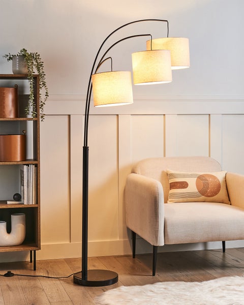 Stehlampe mit drei Lampenschirmen neben Sessel und Regal