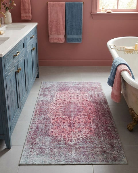Rechteckiger Badteppich mit orientalischem Vintage-Muster in Rosa und Violett in einem hellen Bad mit blauem Waschtisch und Badewanne.