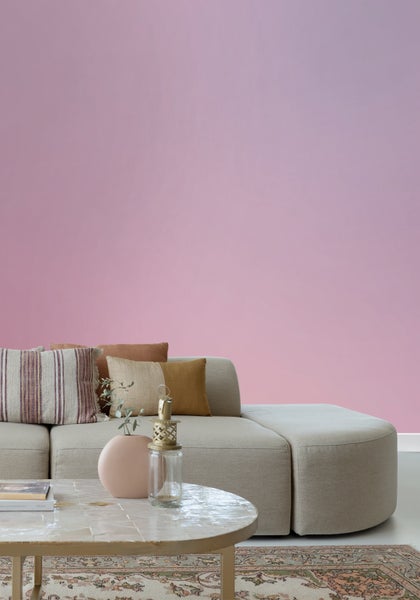 Wohnzimmer mit Couch, Kissen und Tisch auf einem Teppich vor einer farbigen Wand