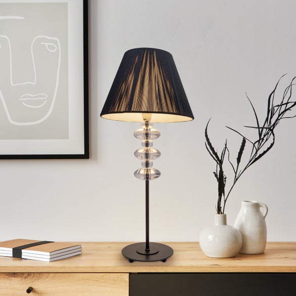 Dekorative Tischleuchte mit schwarzem Schirm und Glaselementen auf einem Holztisch