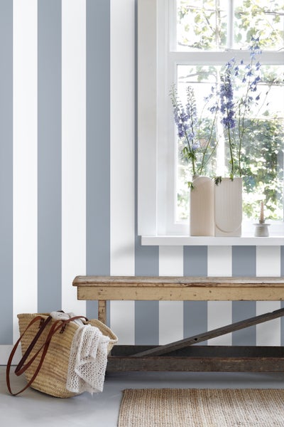 Gestreifte Tapete in einem hellen Zimmer mit rustikaler Holzbank, Fenster und Blumenvasen im Landhausstil.