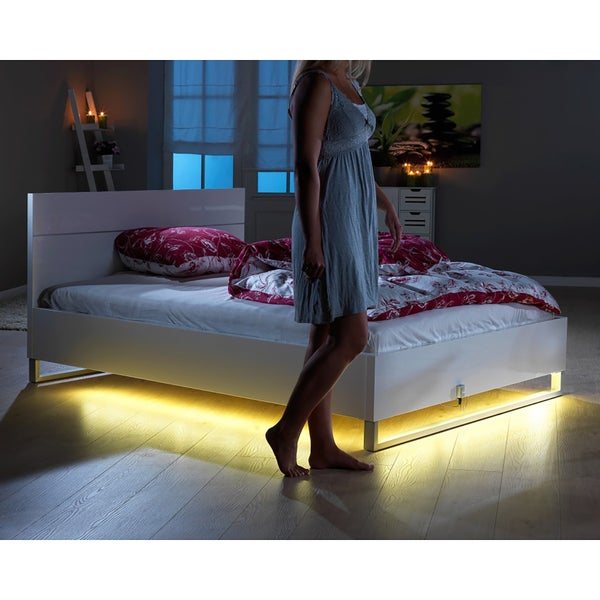 Blick in ein Schlafzimmer mit einem Bett, das mit einer LED-Leuchte beleuchtet wird, während eine Person darauf zugeht