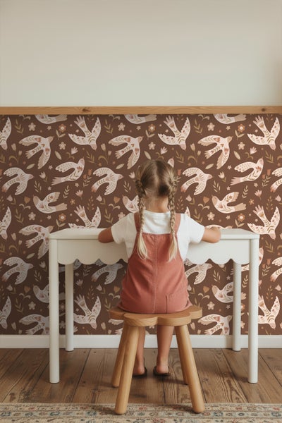 Kind sitzt an einem Schreibtisch vor einer Wand mit Vogelmuster