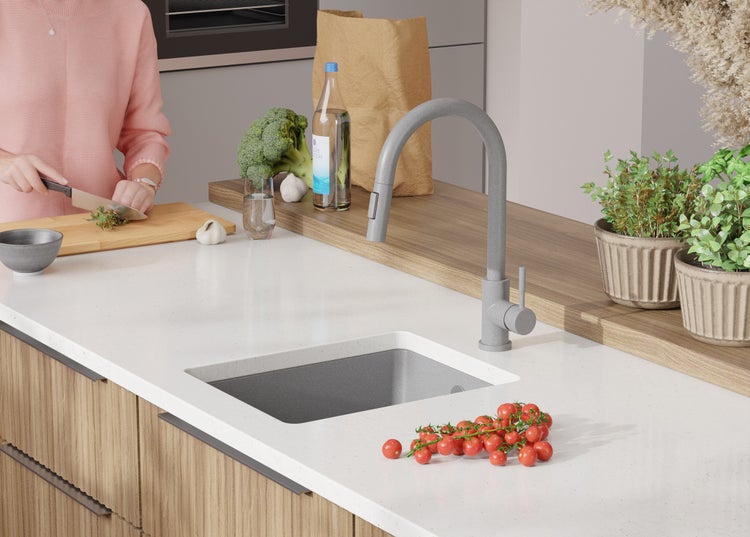 Küchenszene mit Spüle, Armatur, Gemüse und Kräutern auf einer hellen Arbeitsplatte