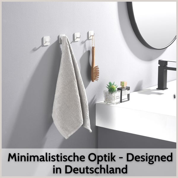 Vier quadratische Wandhaken im Badezimmer, einer mit einem grauen Handtuch und einer mit einer Holzbürste behängt.