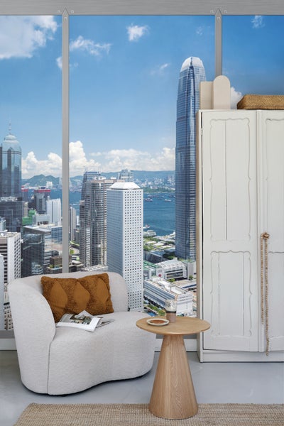 Helles Wohnzimmer mit Sessel, Beistelltisch und Kleiderschrank vor grosser Fensterfront mit Stadtblick