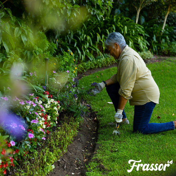 Eine Person mit Gartenhandschuhen nutzt eine Handschaufel zur Pflege eines Blumenbeets an einem Rasen. Frassor Logo.