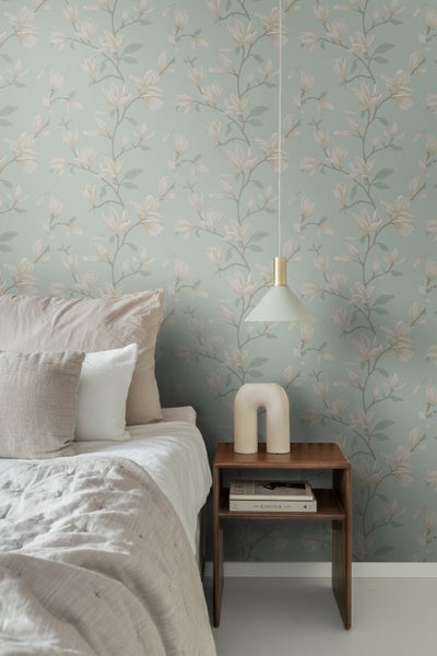 Schlafzimmer mit Bett, Nachttisch und Tapete mit floralem Muster