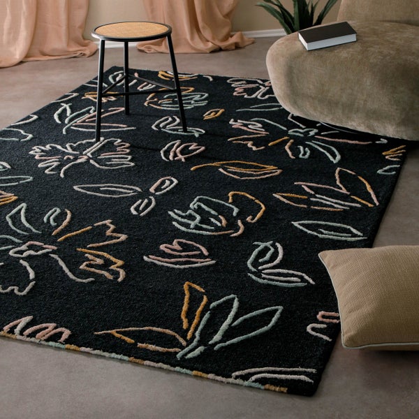 Moderner rechteckiger Teppich mit abstrakten floralen Mustern in einem hellen Wohnzimmer neben einem Hocker und Sessel.