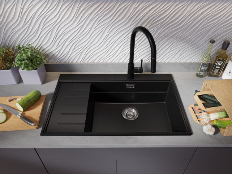 Schwarzes Spülbecken mit Abtropffläche und Armatur auf einer Küchentheke mit Gemüse