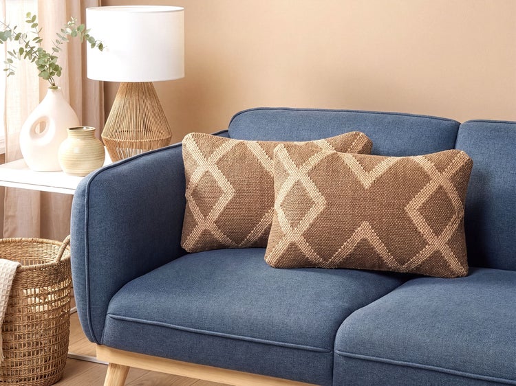 Zwei rechteckige Zierkissen mit Rautenmuster auf einem Sofa in einem modern eingerichteten Wohnbereich mit Tischlampe und Pflanze.