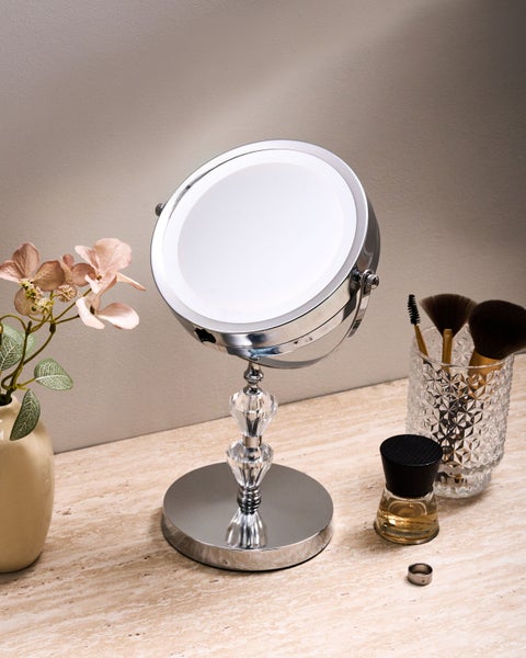 Kosmetikspiegel mit LED-Beleuchtung auf einem Tisch mit Blumen und Kosmetikpinseln