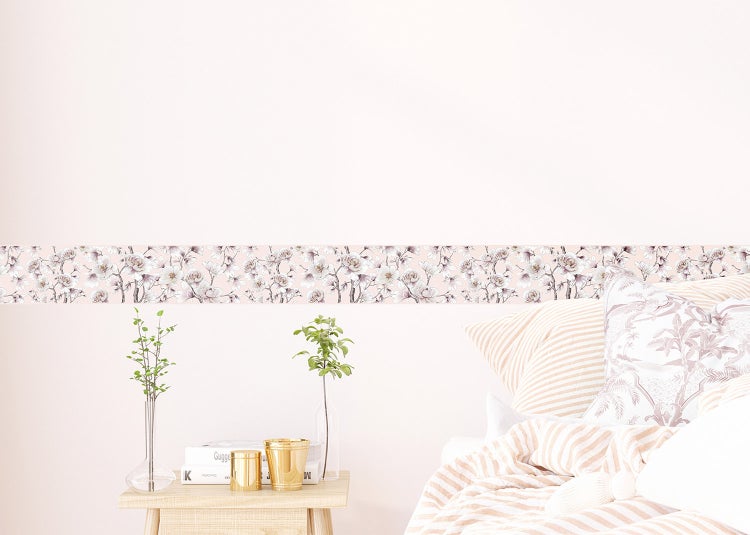 Tapetenbordüre mit floralem Magnolien-Muster in einem hellen Schlafzimmer über einem Nachttisch mit Dekoration und einem Bett.