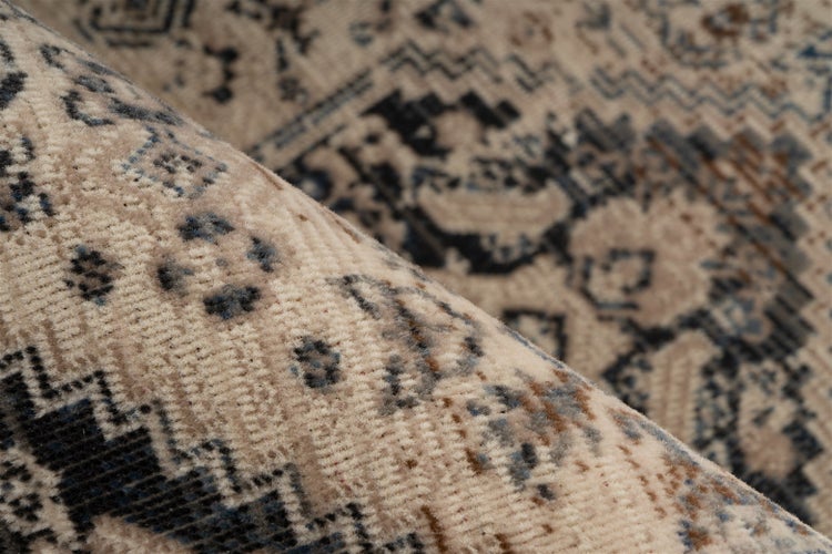 Nahaufnahme eines Teppichs mit orientalischem Muster in Creme und Blau, gefaltet zur Ansicht der Textur.