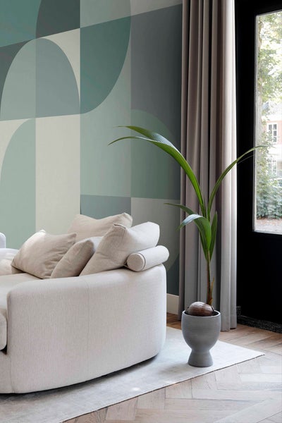 Wohnzimmer mit Sofa, Kissen, Pflanze und geometrischer Tapete für eine helle und organisierte Atmosphäre.
