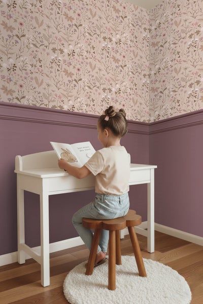 Ein Mädchen sitzt an einem Schreibtisch und liest ein Buch in einem Zimmer mit Blumentapete