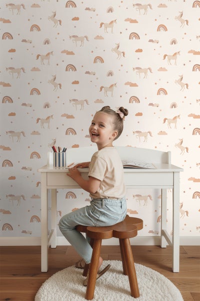 Mädchen sitzt an einem Schreibtisch vor einer Wand mit Einhorn Tapete