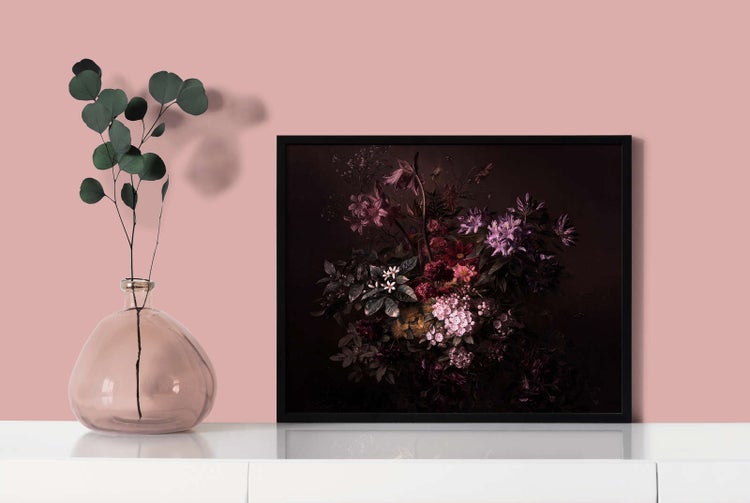 Ein schwarz gerahmtes Bild mit dunklem Blumenmotiv steht auf einer weißen Fläche neben einer Glasvase mit Eukalyptuszweig.