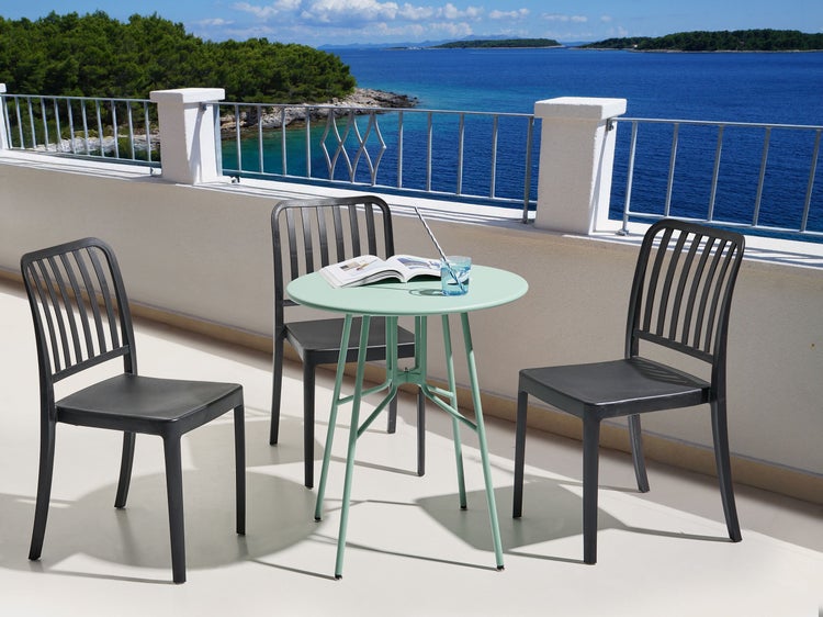 Balkonszene mit Tisch, Stühlen, Buch und Getränk vor Meereskulisse