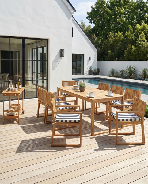 Modernes Gartenmöbel-Set aus Holz auf einer Terrasse mit Pool. Bestehend aus einem Esstisch, Stühlen mit gestreiften Kissen und einem Servierwagen.