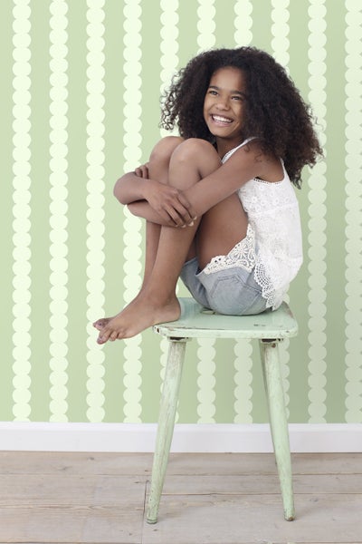 Mädchen mit lockigem Haar sitzt auf einem Hocker vor einer strukturierten Wand