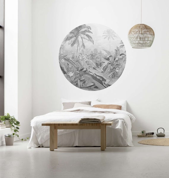 Schlafzimmer mit Bett, Holzboden, Bank, Zimmerpflanze, Hängelampe und einem Wandbild mit Dschungelmotiven.