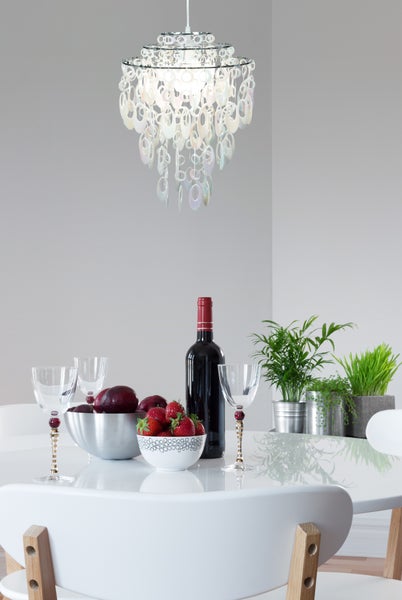 Esstisch mit Dekoration, bestehend aus einer Lampe, Pflanzen, Geschirr, Obst und einer Weinflasche