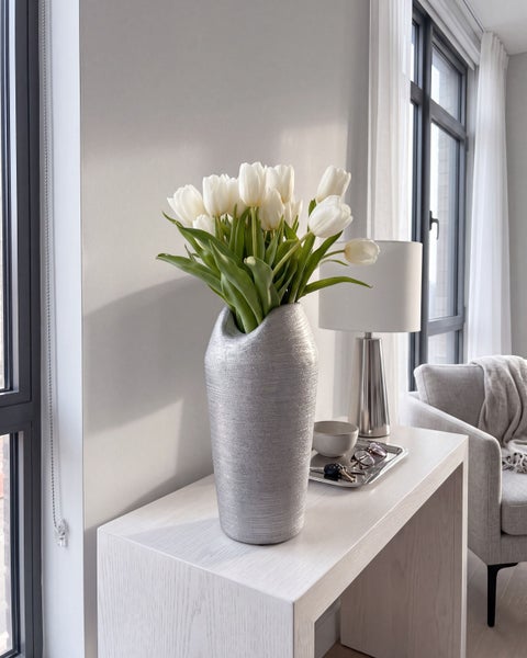 Strukturierte Dekovase in Silberoptik mit einem Blumenstrauß aus Tulpen auf einer Konsole in einem hell eingerichteten Wohnzimmer.