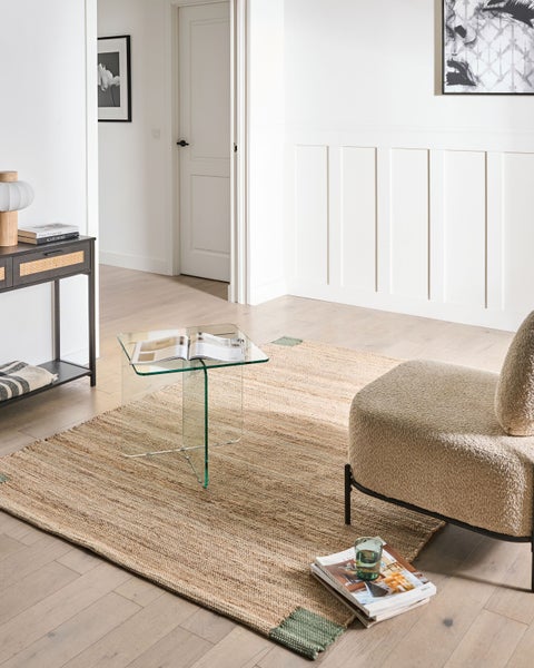 Helles, modernes Wohnzimmer mit gewebtem Teppich, gläsernem Beistelltisch und strukturiertem Sessel auf hellem Holzboden.