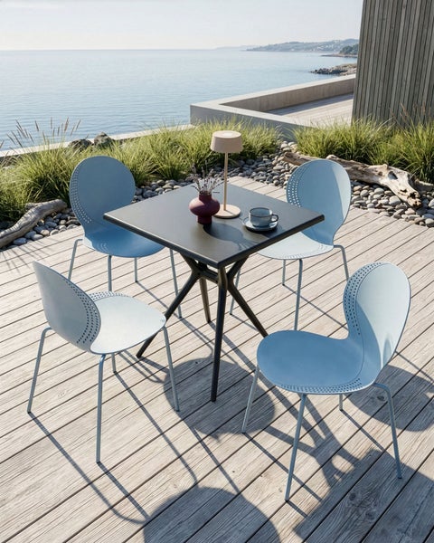 Quadratischer Gartentisch mit vier Stühlen auf einer Holzterrasse mit Meerblick