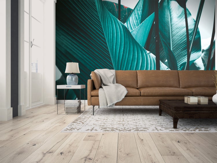 Fototapete mit grünem Blattmotiv in einem hellen Wohnzimmer mit Ledersofa und Holzboden.