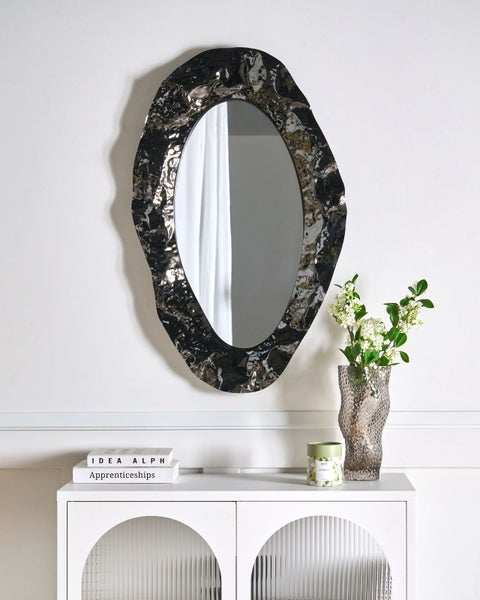 Ovaler Wandspiegel mit unregelmäßig geformtem Rahmen über einem weißen Schrank