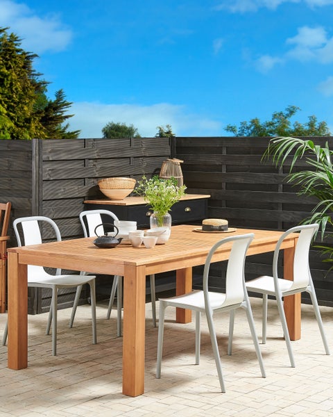 Gartenszene mit Holztisch, Stühlen, Geschirr und Pflanzen für eine einladende Atmosphäre im Freien