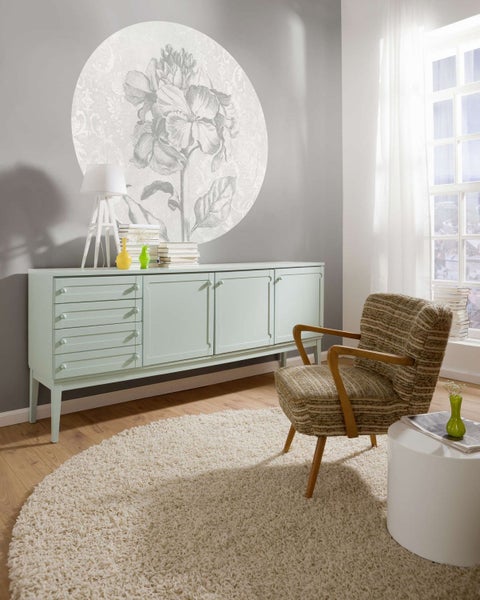 Wohnzimmer mit mintgrünem Sideboard, Sessel, rundem Teppich und Wandbild