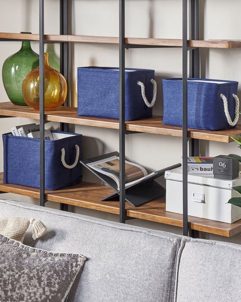Blaue Aufbewahrungsboxen aus Textil mit Seilgriffen in einem Regal aus Holz und Metall neben Glasvasen und Büchern.