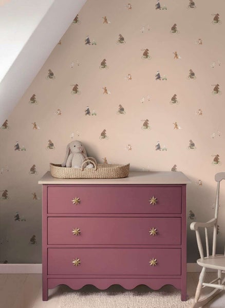 Kindertapete mit Tiermotiven an einer Wand hinter einer violetten Kommode mit Stoffsitz und Kuscheltier in einem Kinderzimmer.