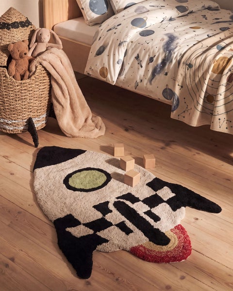 Kinderzimmer mit einem Raketenformteppich, Holzboden und Bett mit Weltraum Bettwäsche.
