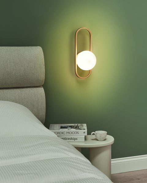 Wandleuchte neben einem Bett mit Nachttisch und dekorativen Büchern.